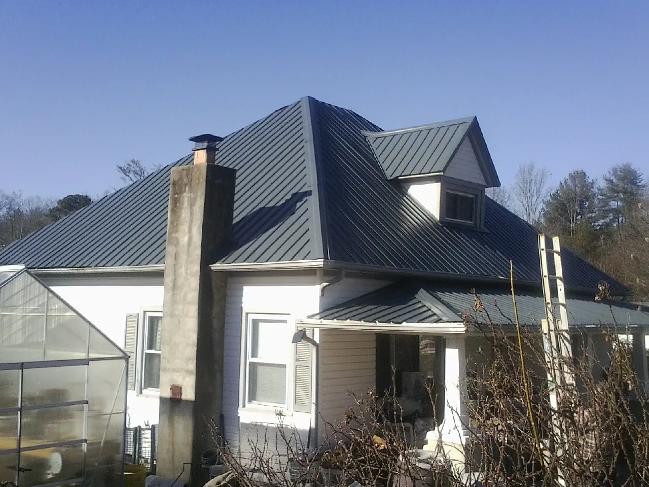 Dark blue standing seam metal roof on a white farmhouse with dormer — Slate & Tile Roof Repair by Roofing Brothers in Elk