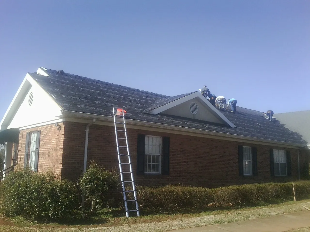 Crew tearing shingles off a brick ranch roof with a ladder set — Emergency Roof Repair work by our crew in Elk