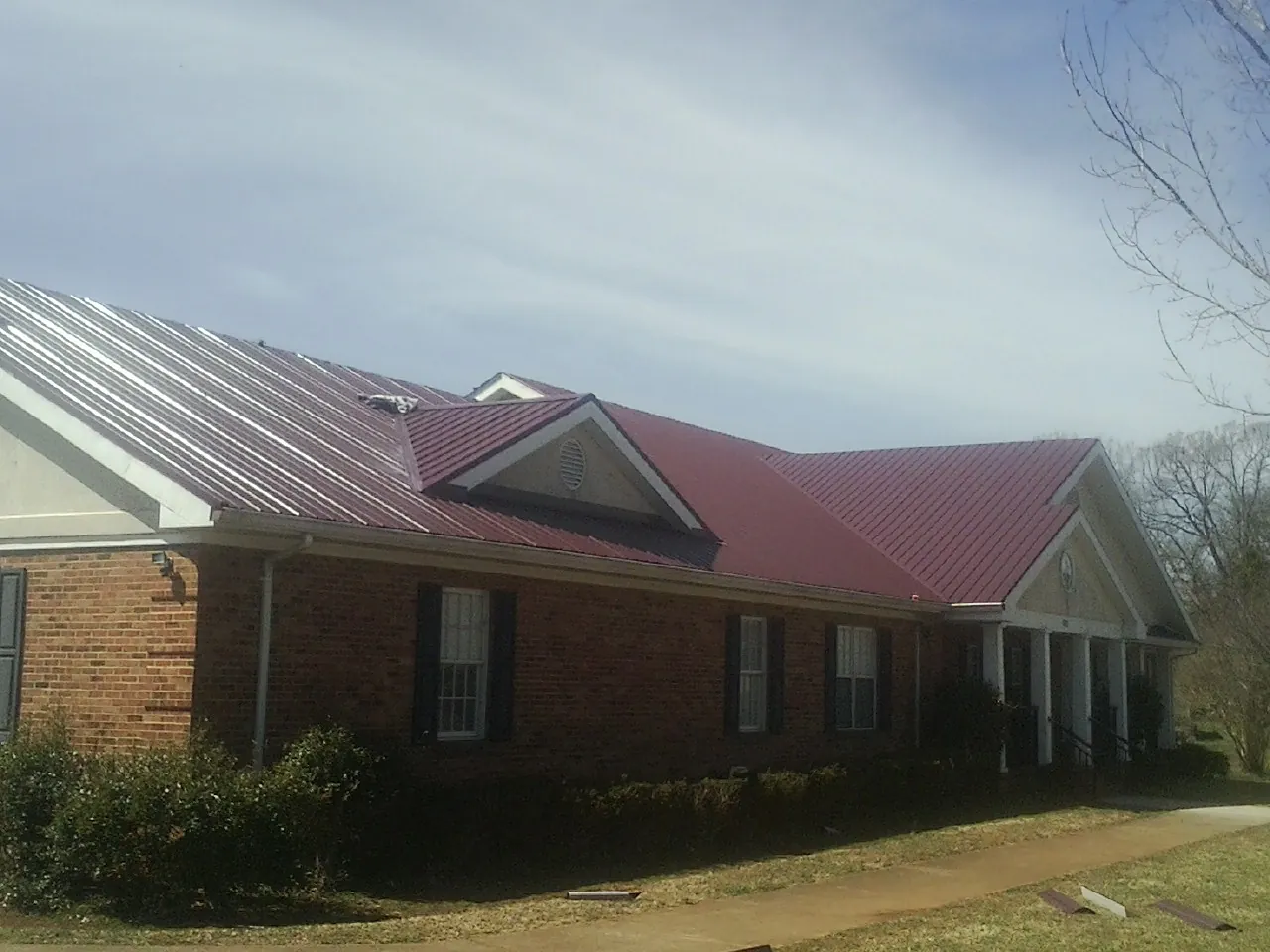 Red metal roof with gabled entries on a long brick building, from a Hail Damage Roof Repair job in Elk