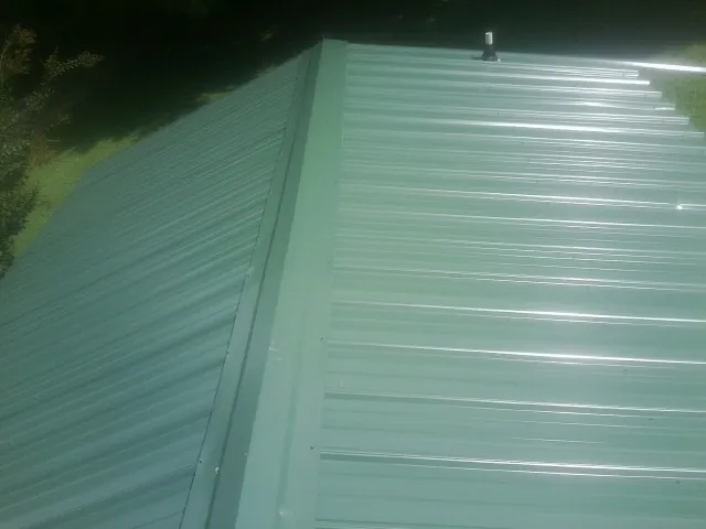 New green metal panels meeting at the ridge of a roof — Flat Roof Repair work by our crew in Elk