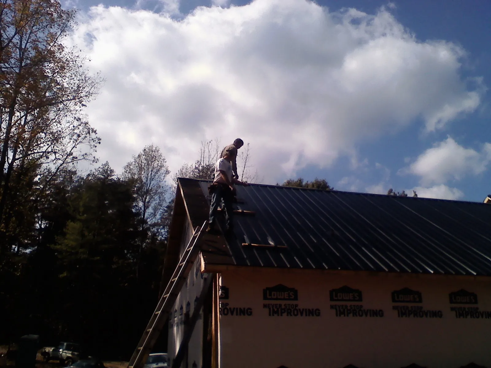 Roofer fastening dark metal panels high against a cloudy sky, from a Roof Inspection job in Elk
