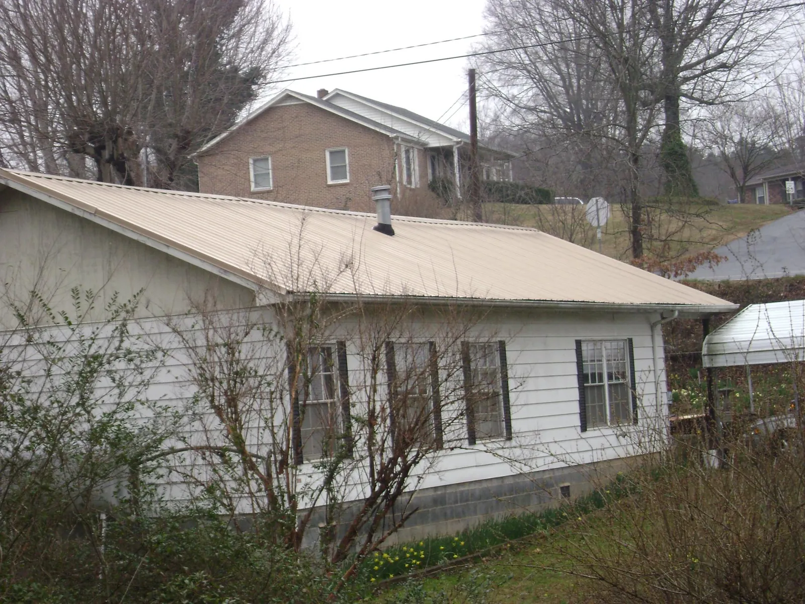 Tan metal roof on a white sided house set into a hillside — Commercial Roofing by Roofing Brothers in Elk