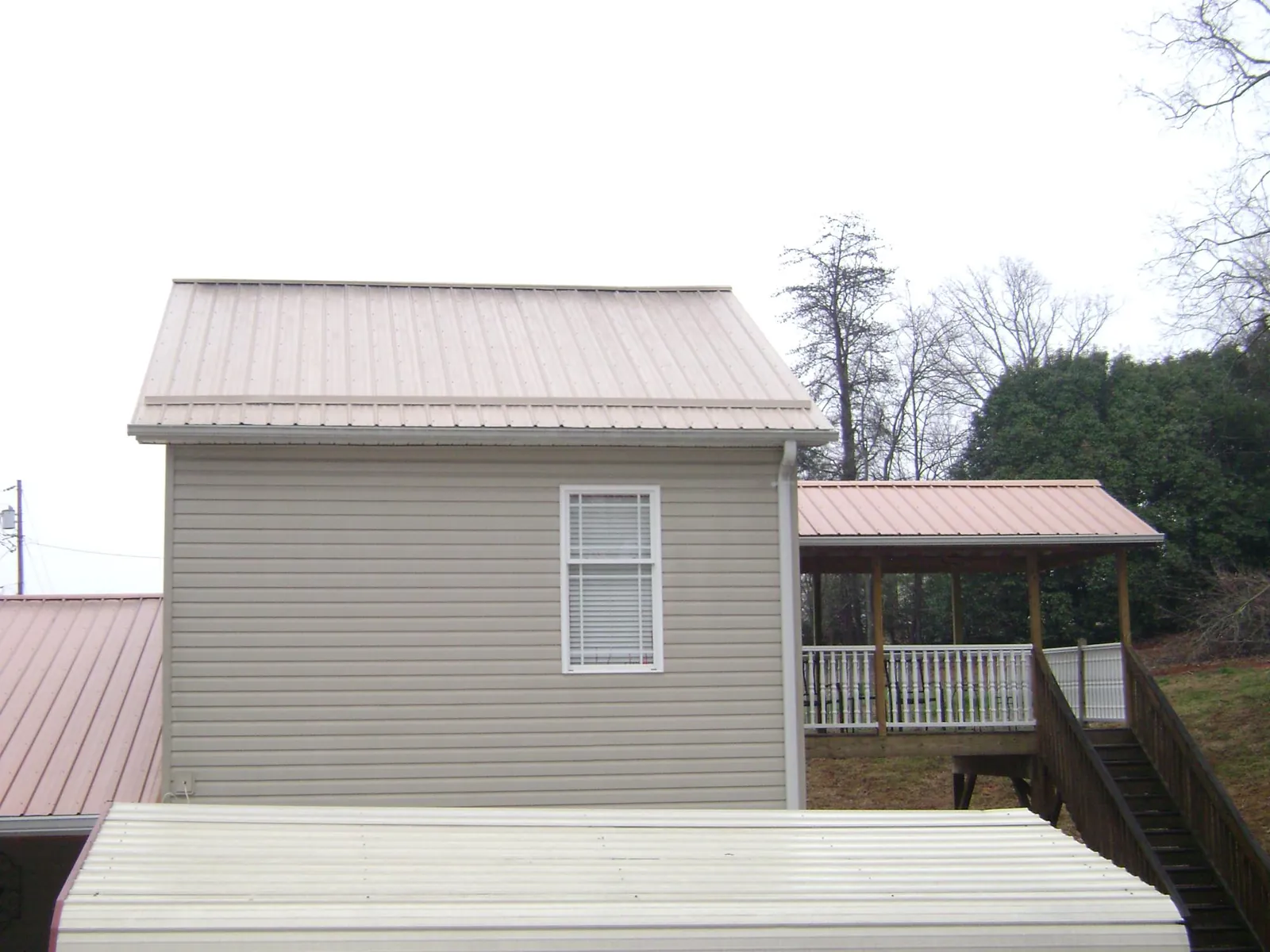 Tan metal roofs on a two story addition and attached porch, from a Roof Replacement job in Elk